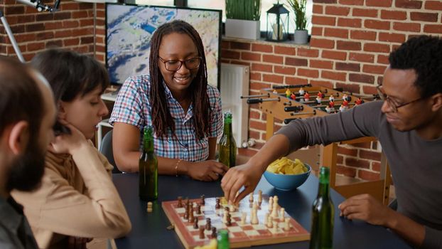 Portrait of cheerful woman sitting with friends at table to play chess board game and have fun together. Happy person smiling while she enjoys gathering with diverse group of people.