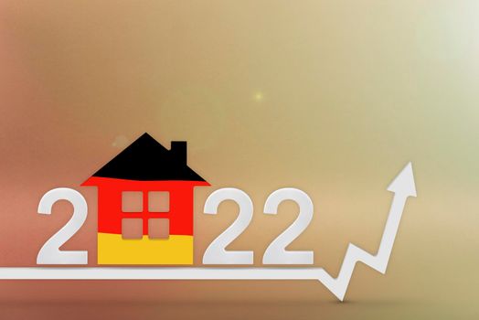 The cost of real estate in Germany in 2022. Rising cost of construction, insurance, rent in Germany. House model painted in flag colors, up arrow on yellow background