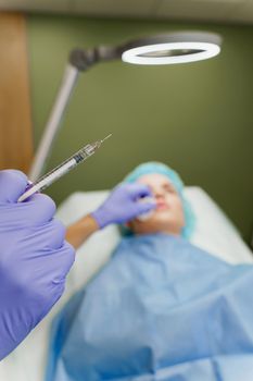 Doctor holds a syringe on the blurred background with patient. Preparation before plastic surgery. Lips Augmentation