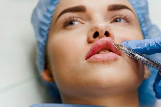 Close-up lips augmentation injections for attractive girl. Plastic surgeon does injection in lip in medical clinic. Cosmetic rejuvenating facial treatment.