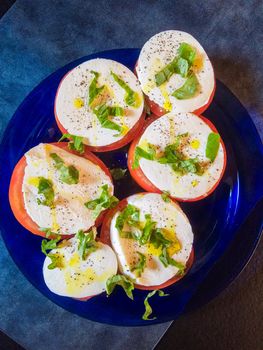 Keto style fresh Italian caprese salad. Mozzarella slices served on slices of beefsteak tomatoes, topped with fresh chopped basil, olive oil, salt and black pepper.