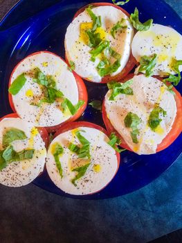 Keto style fresh Italian caprese salad. Mozzarella slices served on slices of beefsteak tomatoes, topped with fresh chopped basil, olive oil, salt and black pepper.