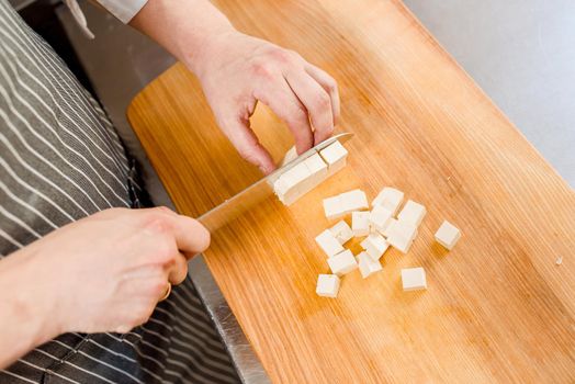 Cut white soft tofu cheese for ramen soup on kitchen . Chef cooks white soft cheese in restaurant. Dice cheese