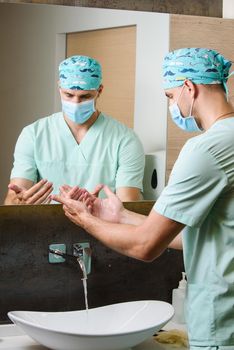 Surgeon looks at the cleanliness of his hands after washing under a stream of water. Wash your hands under running water.