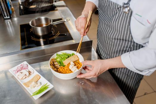 White soft cheese is put on plate. Chef cooks spaghetti noodles for ramen soup. Cooking ramen soup with meat, mushrooms, radish, eggs.