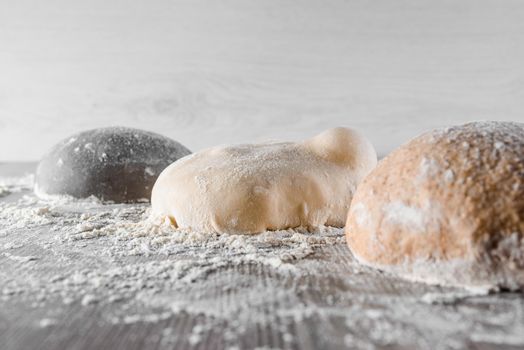 3 dough balls with flour. Cooking black pizza with italian white, yellow, black dough. Food blanks in restaurant.