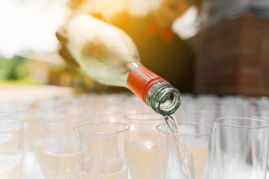 Pouring sparkling wine into glass close up with sun light. Waiter pours champagne into wine glass. Welcome drink zone.