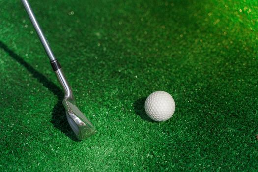 Close-up golf sport game with niblick and white ball on the green grass. Playing in mini golf. Empty place for advert right side.