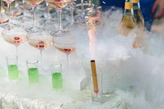 Cold fountain candle burns and dry ice smoke near pyramid of champagne. Beginning of wedding ceremony.