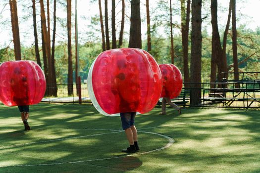 Bubble football sport game. Football players play bumperball on the green field. Team building. Man in bubble balloon run.