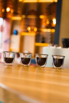 4 Flavored coffee espresso in double glass cup with sun light on background in cafe. Coffee on the wooden table with blurred background.