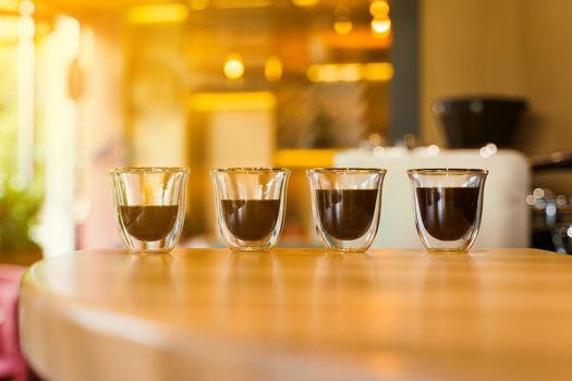 4 Flavored coffee espresso in double glass cup with sun light on background in cafe. Coffee on the wooden table with blurred background