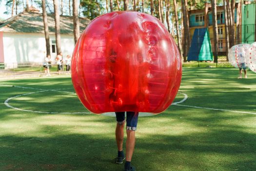 Bubble football sport game. Football players play bumperball on the green field. Team building. Man in bubble balloon run.