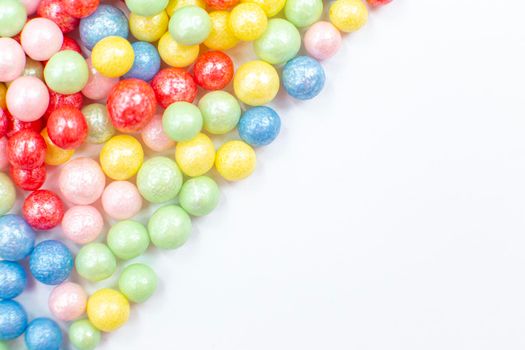 Multi-colored round glossy balls of sugar confectionery lie diagonally to the left on a white background. copy space.