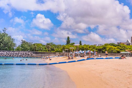 okinawa, japan - september 15 2018: vacationers in swimsuit tanning and having fun on the beach supervised by a lifeguard on the sandy beach Naminoue topped by a highway passing in Naha City in Okinawa Prefecture, Japan.