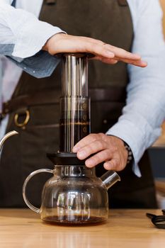 Aeropress coffee close-up: barista press to device and coffee drops pours trought aeropress to pot. Alternative coffee brewing method. Vertical photo