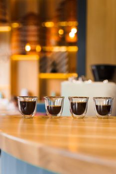 4 Flavored coffee espresso in double glass cup with sun light on background in cafe. Coffee on the wooden table with blurred background.