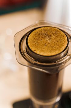 Coffee aeropress creams close-up vertical photo. Alternative coffee brewing method. Aeropress device on the table