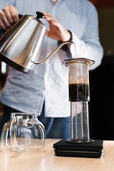 Aeropress coffee close up alternative making by barista in the cafe vertical photo. Barista pours hot water in pot for making aeropress coffee.