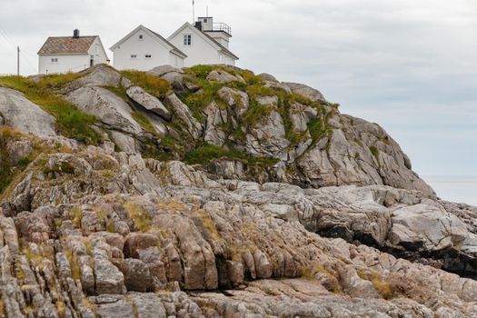 Several white houses stand on the rocky coast of Norway, rocky coast with dramatic sky, the sun breaks through the clouds, sheer cliff. High quality photo