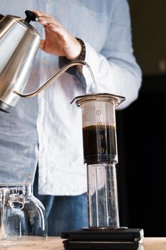 Aeropress coffee close up alternative making by barista in the cafe vertical photo. Barista pours hot water in pot for making aeropress coffee.