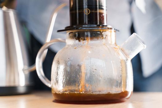 Aeropress coffee and glass pot close-up: barista press to device and coffee drops pours trought aeropress to pot. Alternative coffee brewing method