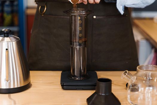 Aeropress coffee: barista spread ground coffee to pot. Alternative coffee brewing method. Handsome bearded barista makes tasty Scandinavian coffee