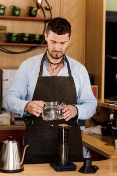 Aeropress coffee and handsome bearded barista in cafe. Barisa cook tasty coffee using alternative brewing method