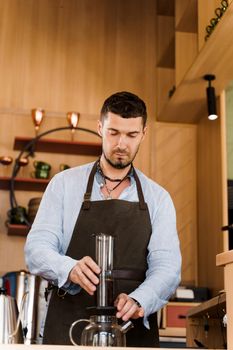 Aeropress coffee and handsome bearded barista in cafe. Barisa cook tasty coffee using alternative brewing method