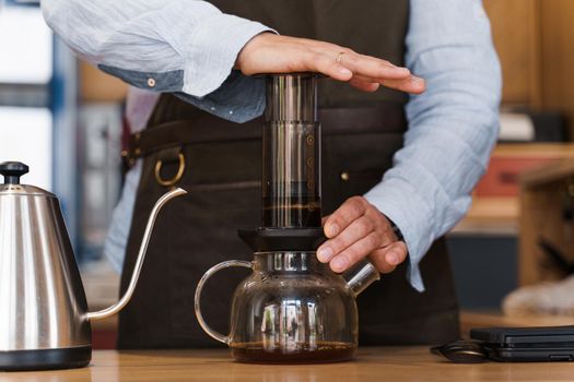 Aeropress coffee close-up: barista press to device and coffee drops pours trought aeropress to pot. Alternative scandinavian coffee brewing method.