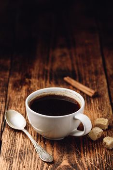 Black coffee in white cup with sugar and cinnamon sticks