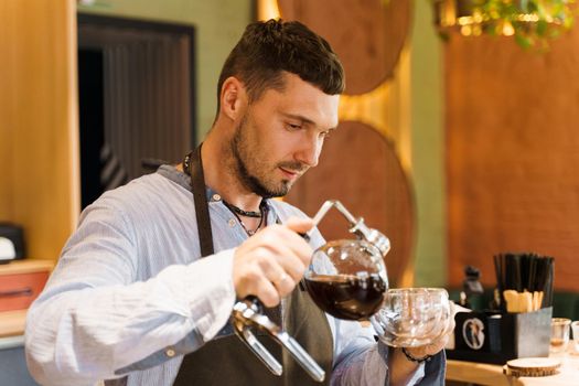 Syphon alternative method of making coffee. Barista pours hot coffee in syphon device for customers. Coffee brewing in cafe