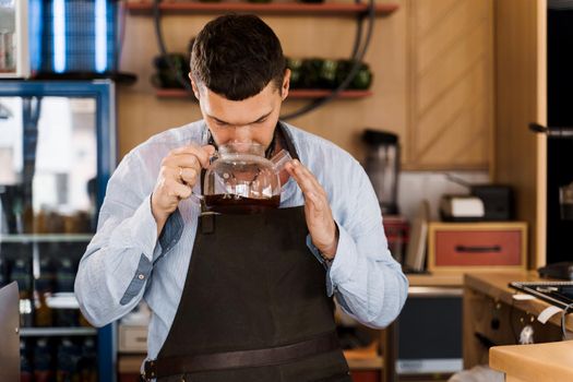 Barista sniffs flavored coffee in glass pot in cafe. Coffee brewing syphon and aeropress alternative methods