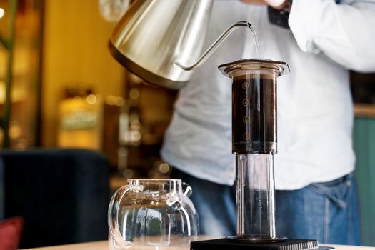 Aeropress coffee close up alternative making by barista in the cafe. Scandinavian coffee brewing method. Barista pours water to aeropress with coffee