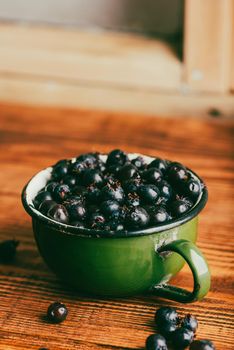 Ripe Purple Amelanchier Berries in Green Metal Cup on Wooden Surface