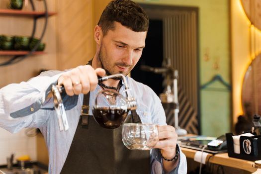 Syphon alternative method of making coffee. Barista pours hot coffee in syphon device for customers. Coffee brewing in cafe