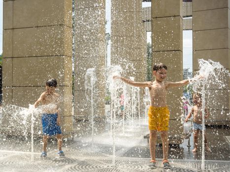 Kyiv, Ukraine - August 01, 2021: Boys jumping in water fountains. Children playing with a city fountain on hot summer day. Happy friends having fun in fountain. Summer weather. Friendship, lifestyle and vacation.