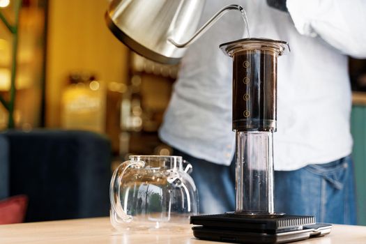 Aeropress coffee close up alternative making by barista in the cafe. Scandinavian coffee brewing method. Barista pours water to aeropress with coffee