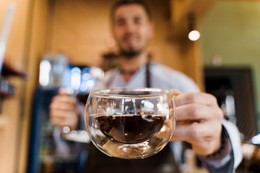 Close-up double glass cup with coffee in cafe. Barista gives a cup of coffee to you. Alternative coffee brewing using Syphon device.