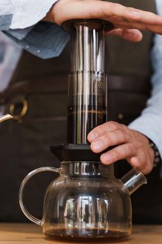 Aeropress coffee close-up: barista press to device and coffee drops pours trought aeropress to pot. Alternative coffee brewing method. Vertical photo