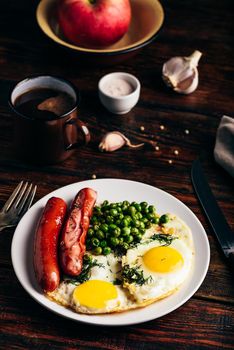 Breakfast with fried eggs, sausages and green peas on white plate