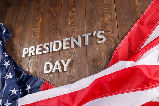 words presitdents day laid with silver metal letters on wooden surface near crumpled US flag