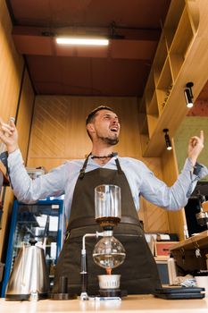 Syphon coffee device with fire heats glass flask in cafe. Emotional barista shows rock and roll. Alternative coffee brewing method