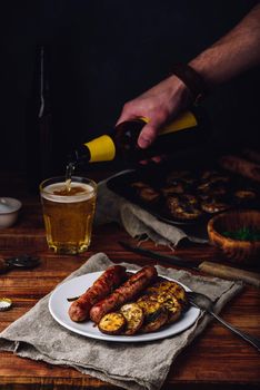 Pork sausages baked with eggplant, leek and herbs on white plate. Man Pouring Beer into a Glass.
