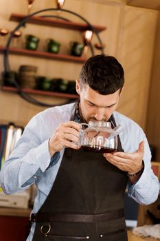 Barista sniffs flavored coffee in glass pot in cafe. Coffee brewing syphon and aeropress alternative methods