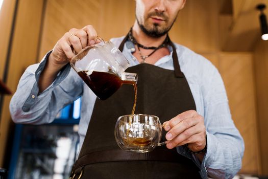 Barista pours flavored coffee in glass pot in cafe. Coffee brewing syphon and aeropress alternative methods