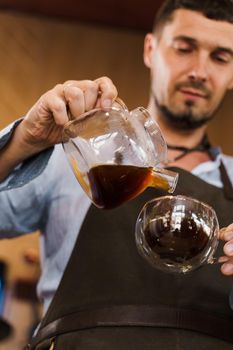 Close-up pouring coffee in double glass cup in cafe by handsome bearded barista. Coffee brewing syphon and aeropress alternative methods