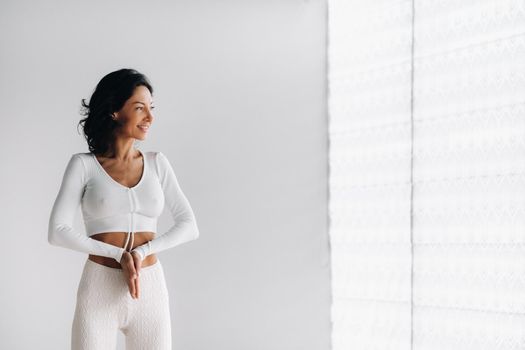 a female yogi in white clothes stands with her hands clasped at the bottom meditating in the yoga hall.