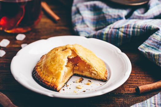 Homemade apple mini pie on white plate with cup of black tea