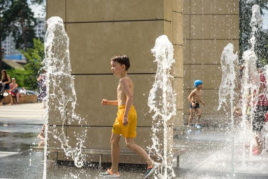 Kyiv, Ukraine - August 01, 2021: Boys jumping in water fountains. Children playing with a city fountain on hot summer day. Happy friends having fun in fountain. Summer weather. Friendship, lifestyle and vacation.